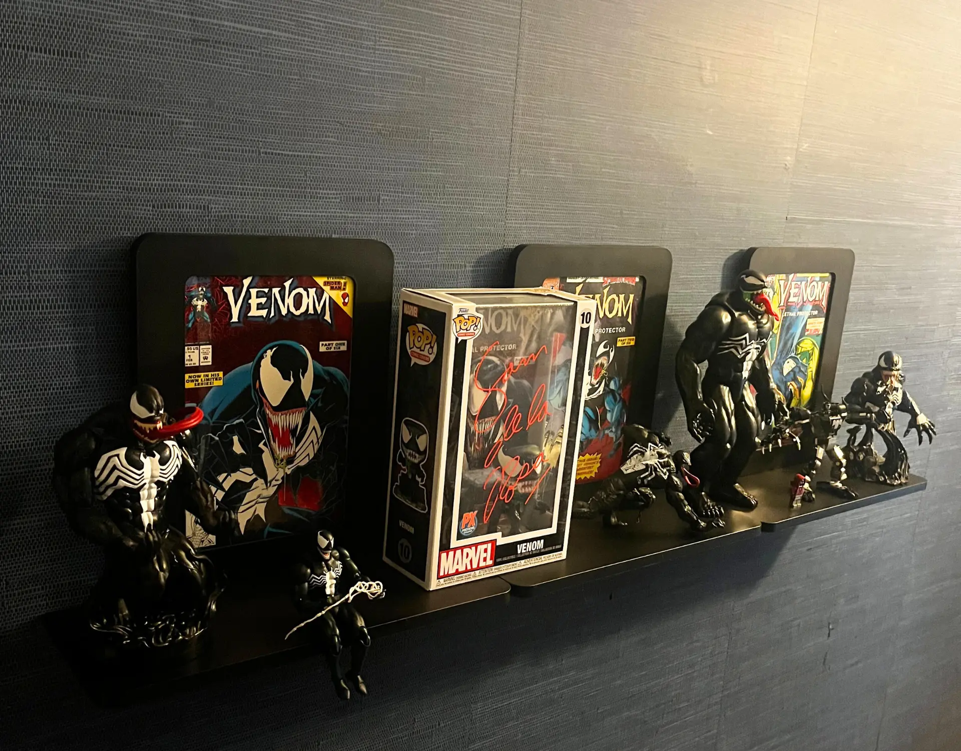 A Venom collection on Nerd Hero shelves: framed Venom Lethal Protector comics, a signed Funko Pop, and Venom figures
